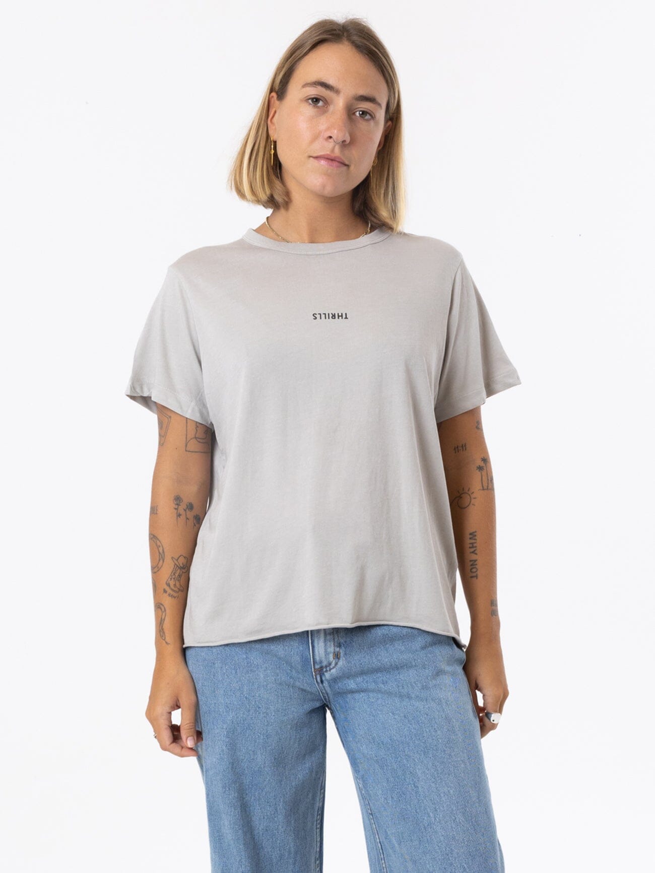 Female model wearing our Thrills Minimal Thrills Relaxed Tee in Grey standing against a plain studio background.