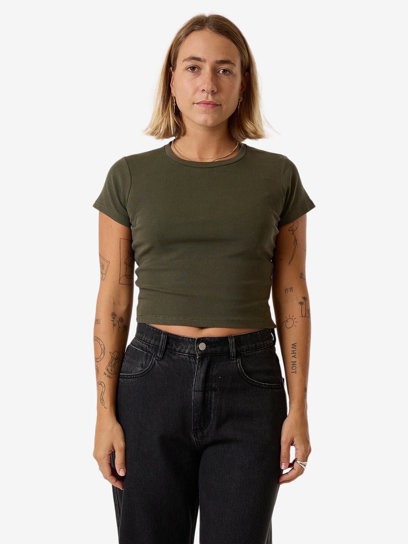 Female model wearing our Thrills Minimal Thrills Mini Tee in Green standing against a plain studio background.