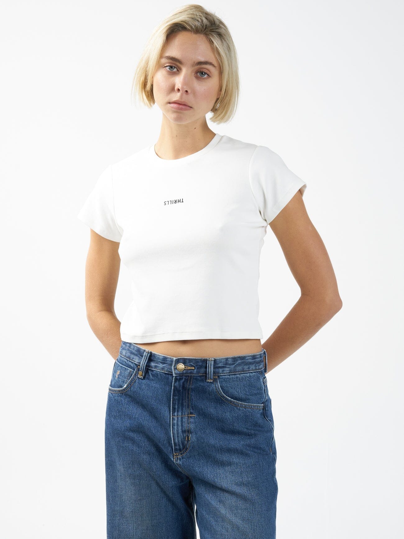 Female model wearing our Thrills Minimal Thrills Mini Tee in White standing against a plain studio background.