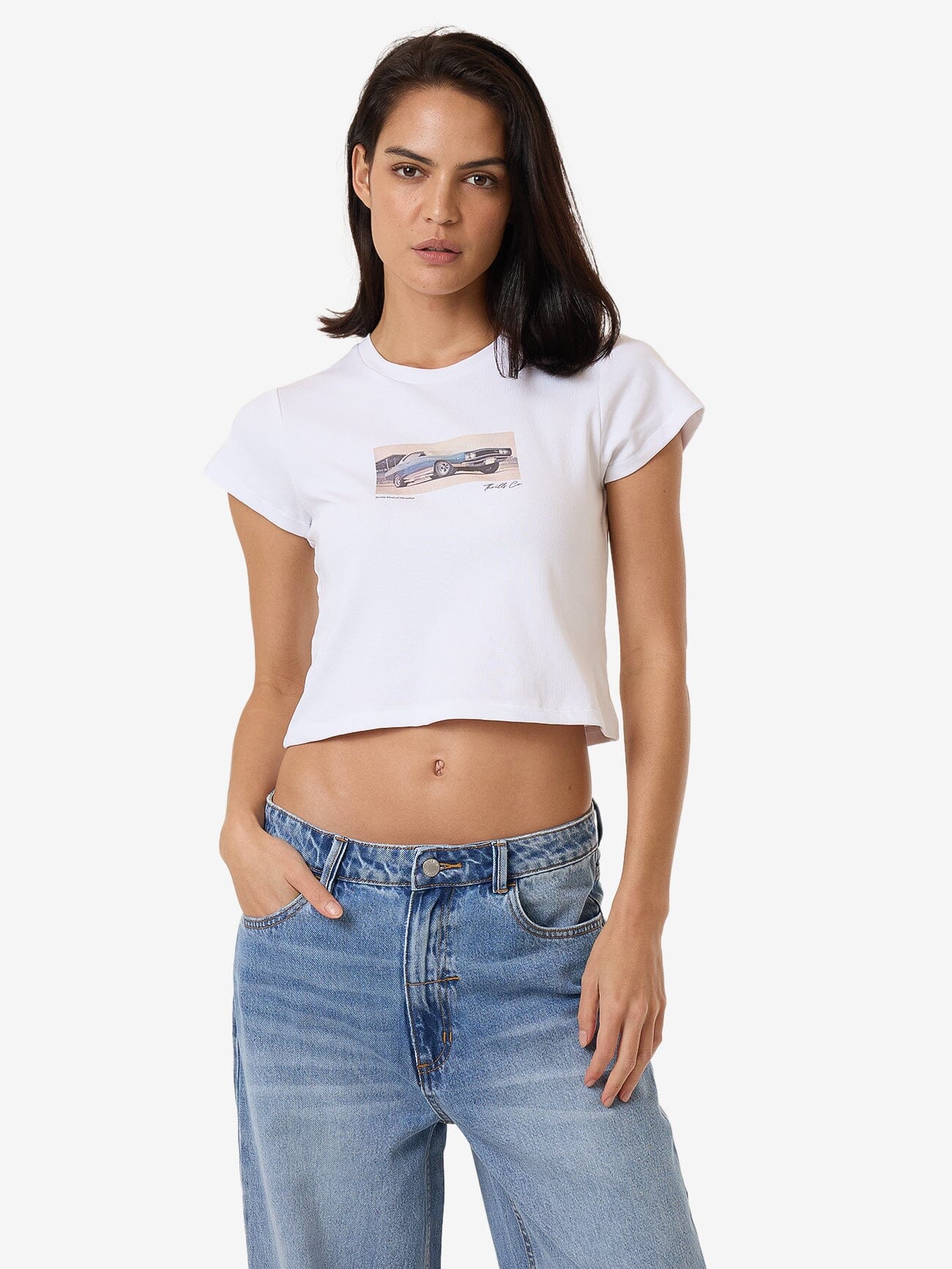 Female model wearing our Thrills Paradise Wheels Mini Tee in White standing against a plain studio background.