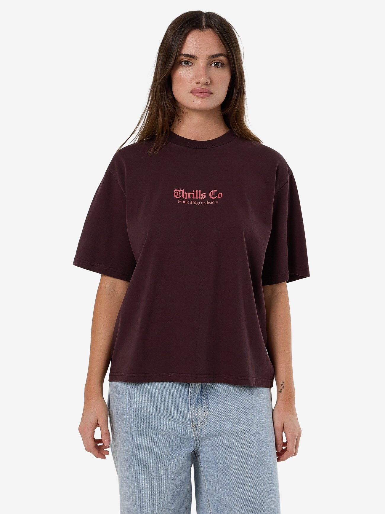 Female model wearing our Thrills Lighten Up Square Tee in Red standing against a plain studio background.