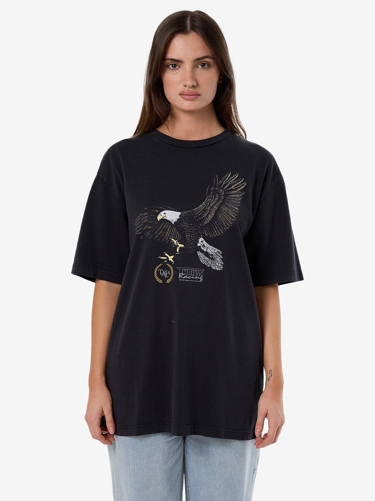 Female model wearing our Thrills Speed Tour Oversized Tee in Black standing against a plain studio background.