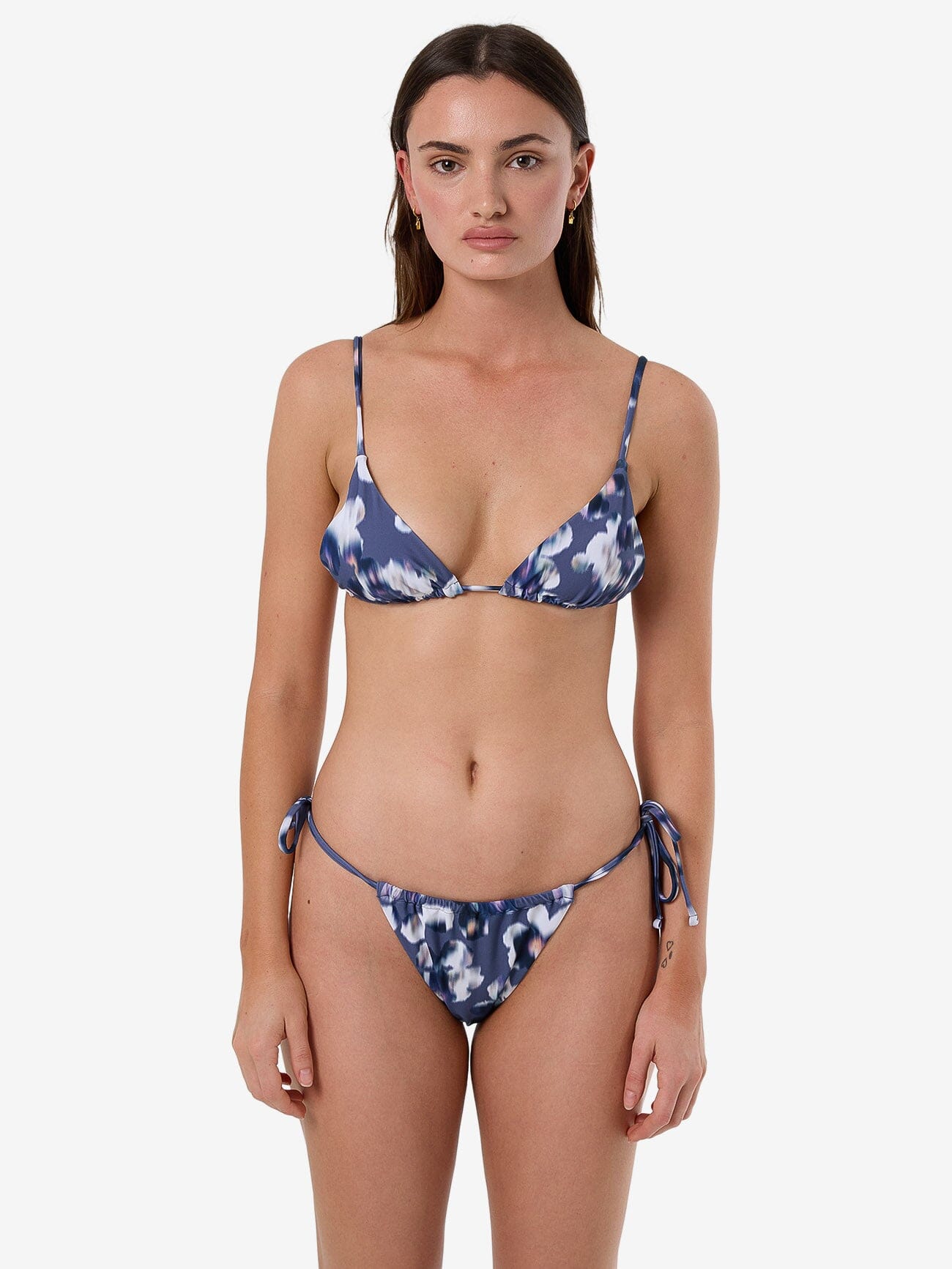 Female model wearing our Thrills Cyber Bloom String Bikini Bottom in Purple standing against a plain studio background.