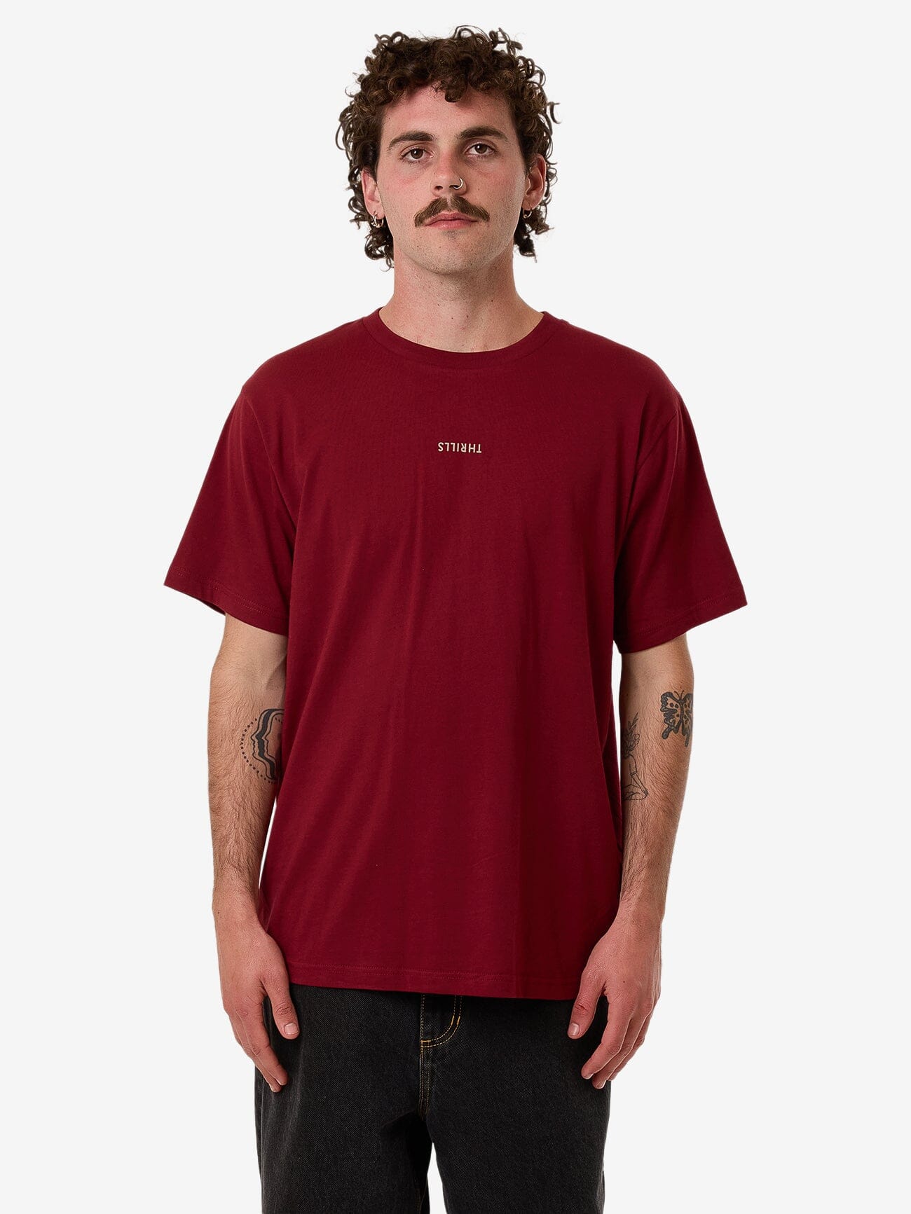 Male model wearing our Thrills Minimal Thrills Merch Fit Tee in Red standing against a plain studio background.