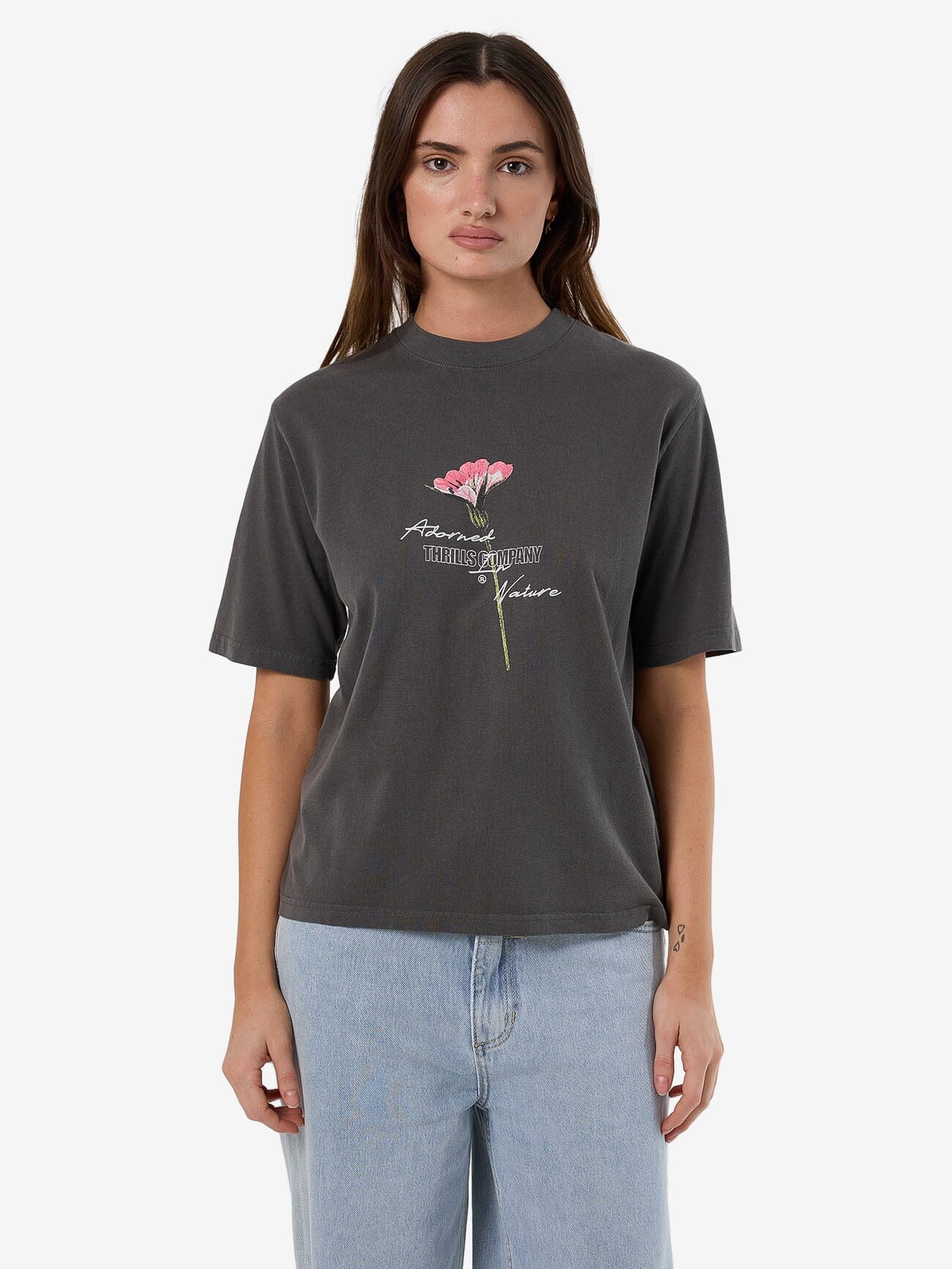 Female model wearing our Thrills  Adorned In Nature Square Tee in Black standing against a plain studio background.