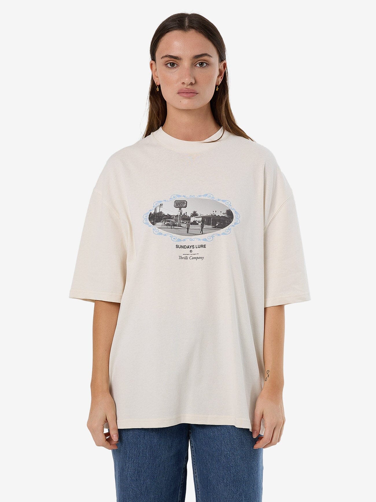 Female model wearing our Thrills  Sundays Lure Oversized Tee in White standing against a plain studio background.